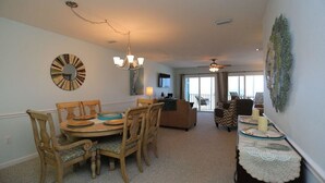 A dining area with a round table, chairs, and a chandelier. There is a sofa and a coffee table in the background.