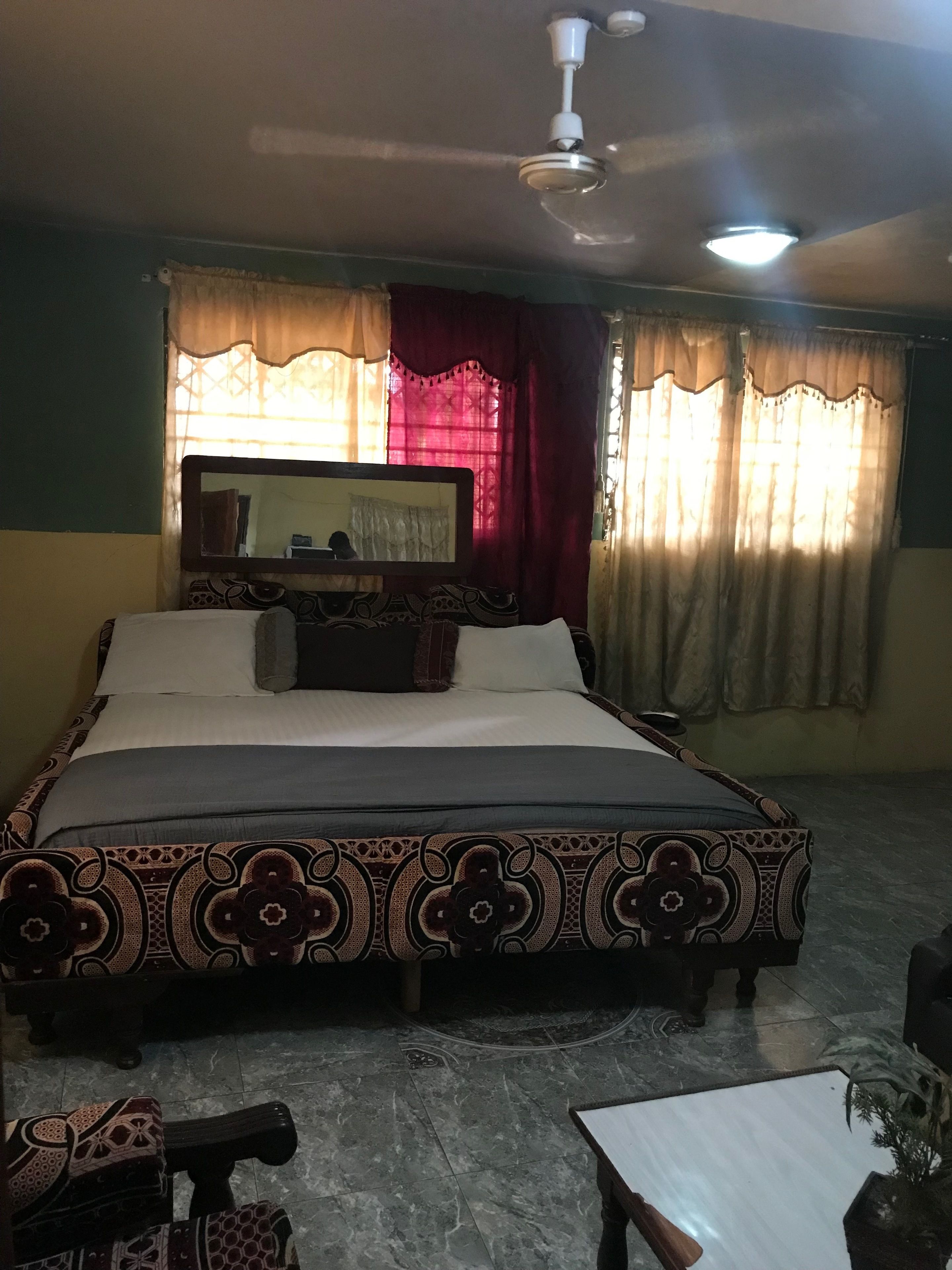 A bedroom with a bed, a ceiling fan, a mirror, and curtains.