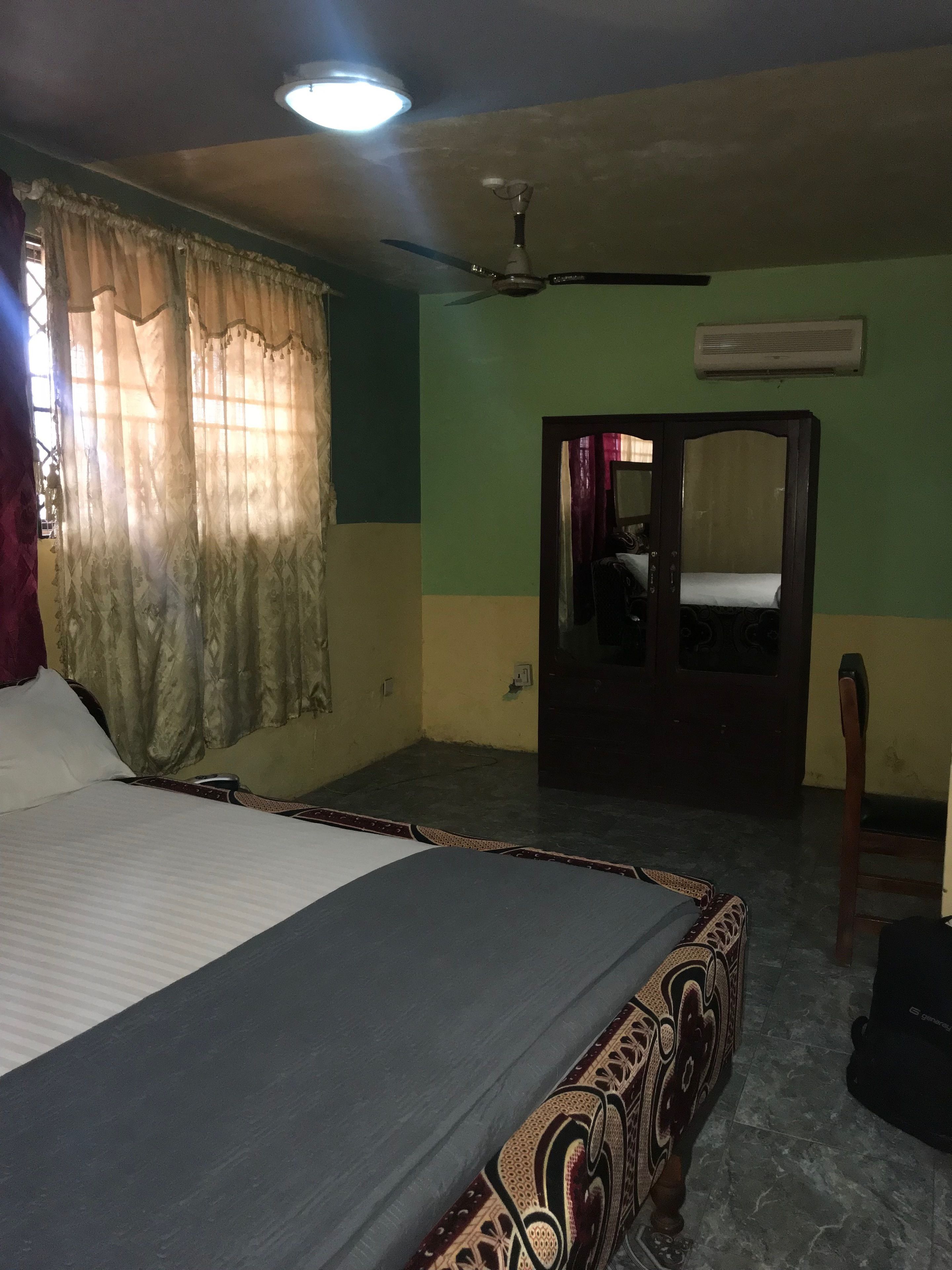 A bedroom with a bed, a ceiling fan, an air conditioning unit, and a mirror.
