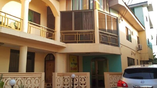 A two-story building with a balcony on the upper floor, a sign indicating a hotel, and a parked car in front. - Heritage Investments Hotel (Accra)