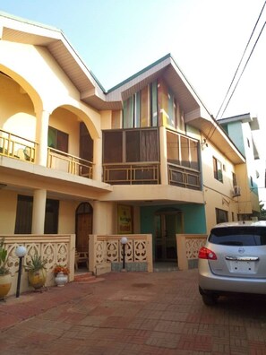 A two-story building with a balcony on the upper floor, a sign indicating a hotel, and a parked car in front. - Heritage Investments Hotel (Accra)