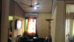 A living room with a ceiling fan, a flat-screen TV, a sofa, a coffee table, and a floor lamp. - Heritage Investments Hotel (Accra)