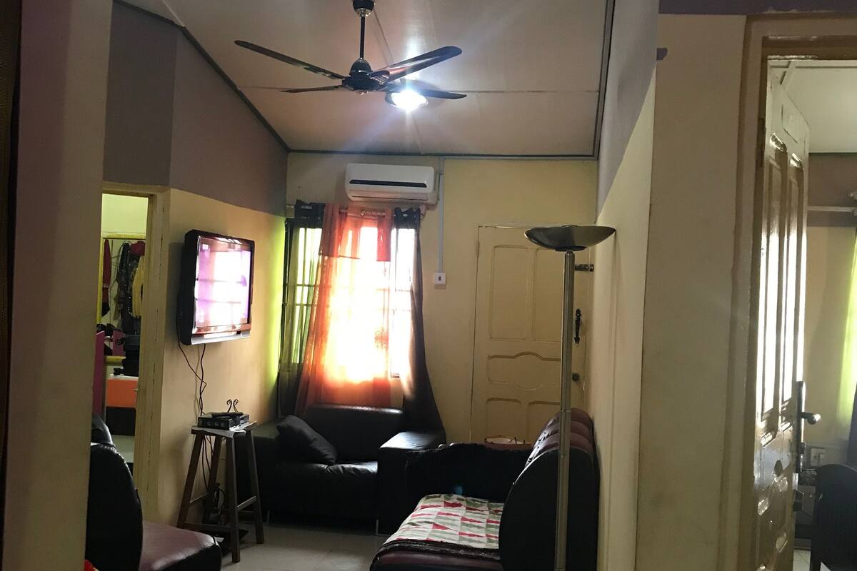 Una sala de estar con ventilador de techo, televisor de pantalla plana, sofá, mesa de centro y lámpara de pie.