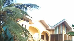 A two-story building with a balcony, a gated entrance, and a palm tree in the foreground. - Heritage Investments Hotel (Accra)