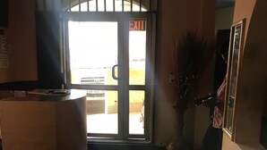 A reception area with a leather sofa, a wooden reception desk, and a glass door with an exit sign. - Heritage Investments Hotel (Accra)