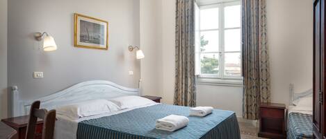 A hotel room with a bed, two bedside tables, a desk, a chair, and a window with curtains.