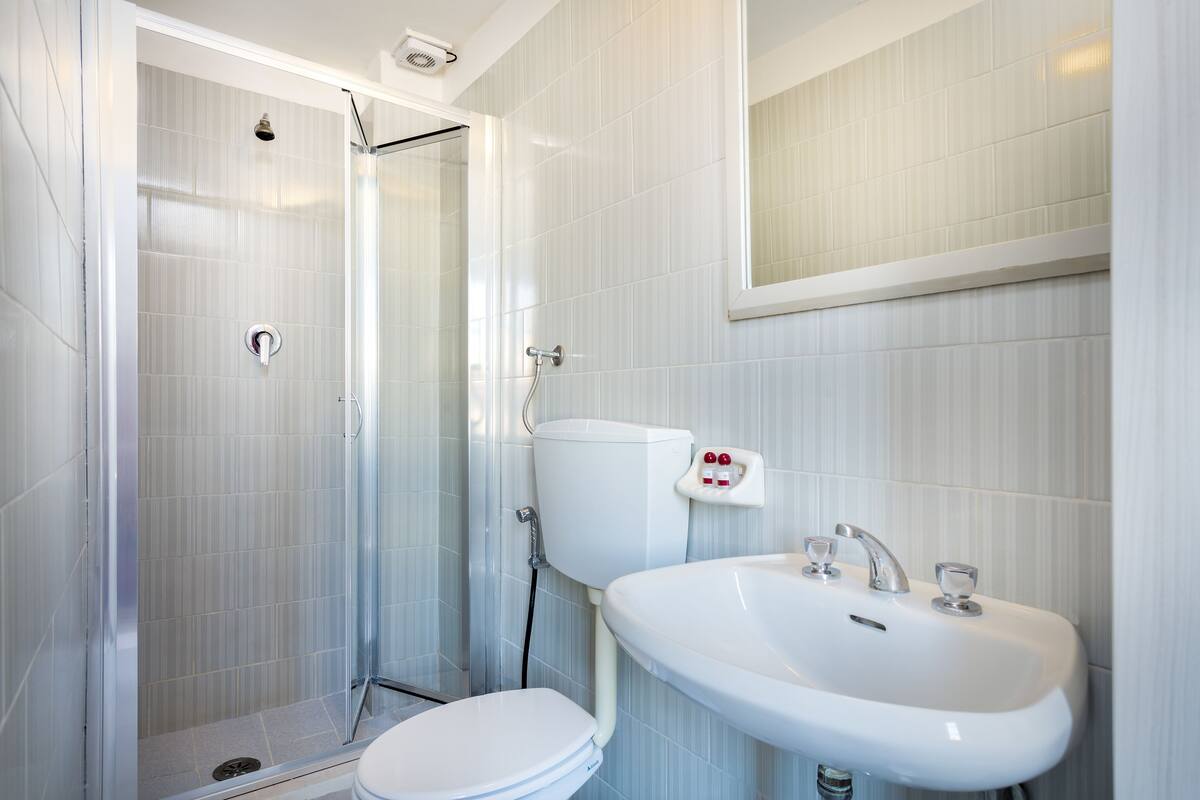 A modern bathroom with a glass-enclosed shower, a white toilet, and a sink with a mirror above it.