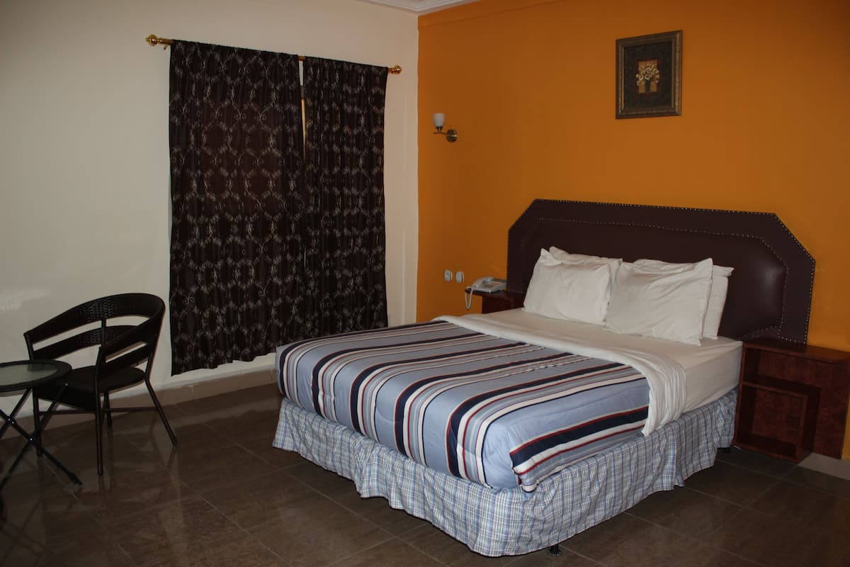 Un dormitorio con cama, una silla, una mesita de noche y una lámpara de pared.