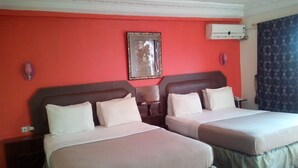 Una habitación de hotel con dos camas, una pared roja y un cuadro enmarcado sobre las camas.