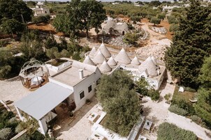 Vista aérea de un patio con estructuras cónicas, un edificio blanco de techo plano y abundante vegetación circundante.