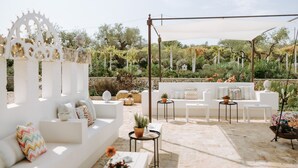 Un área de patio al aire libre con sofás blancos, mesitas y plantas en macetas.