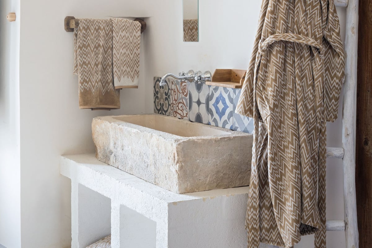 A bathroom with a stone sink, a wooden ladder, and a towel rack with patterned towels.