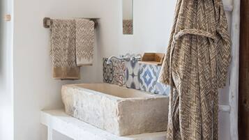 Un baño con un lavabo de piedra, una escalera de madera y un perchero con toallas estampadas.