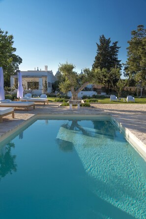 A clear pool with lounge chairs and umbrellas, surrounded by greenery and a building with domed roofs. - Tenuta del Lauro (Locorotondo)