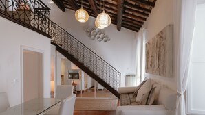 Uma sala de estar ampla com uma mesa de jantar de vidro, sofás brancos, escada de madeira e iluminação decorativa.