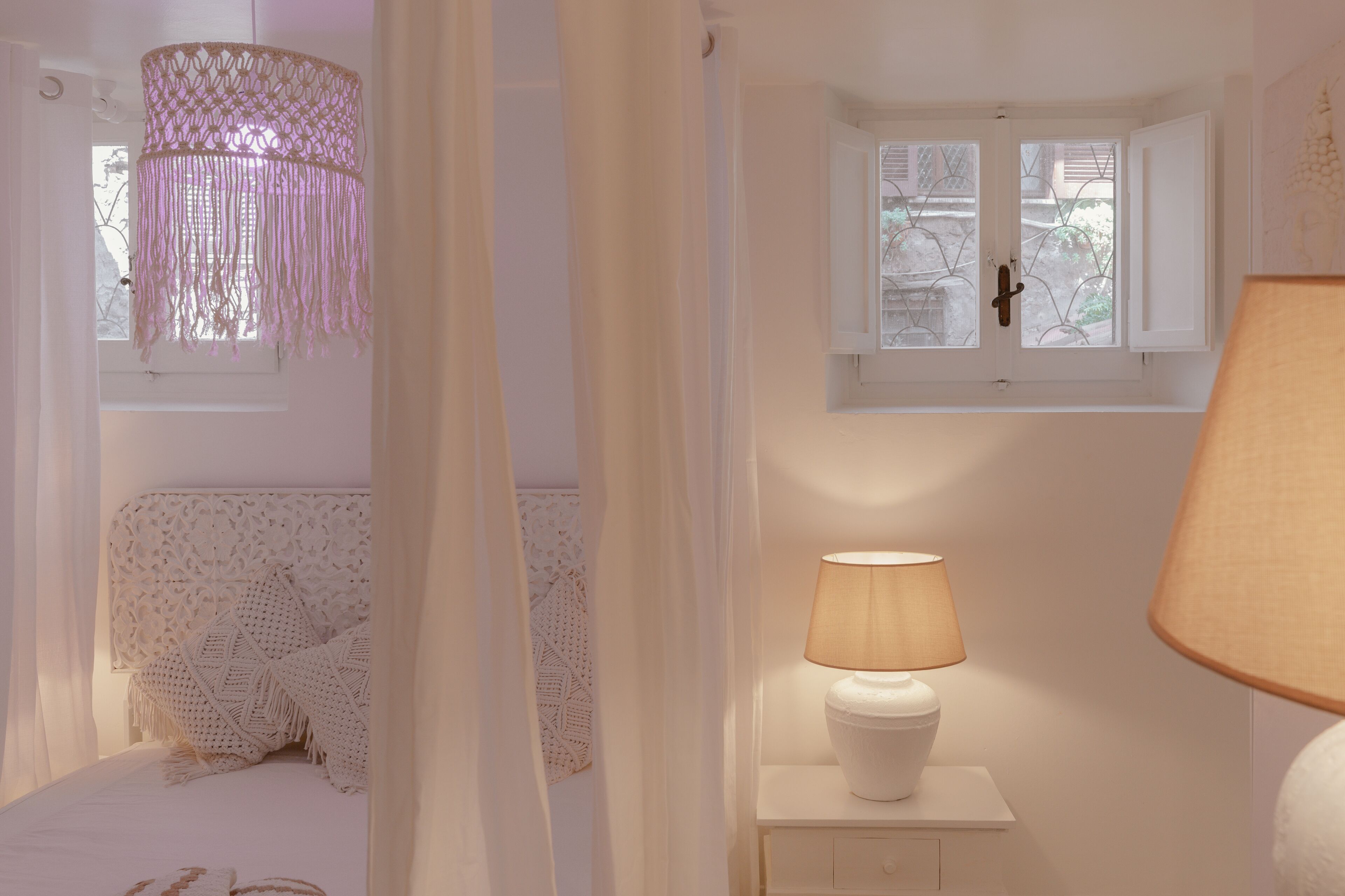 Une chambre à coucher comprenant un lit, une table de chevet avec une lampe, une fenêtre avec des rideaux et un luminaire décoratif suspendu au plafond.