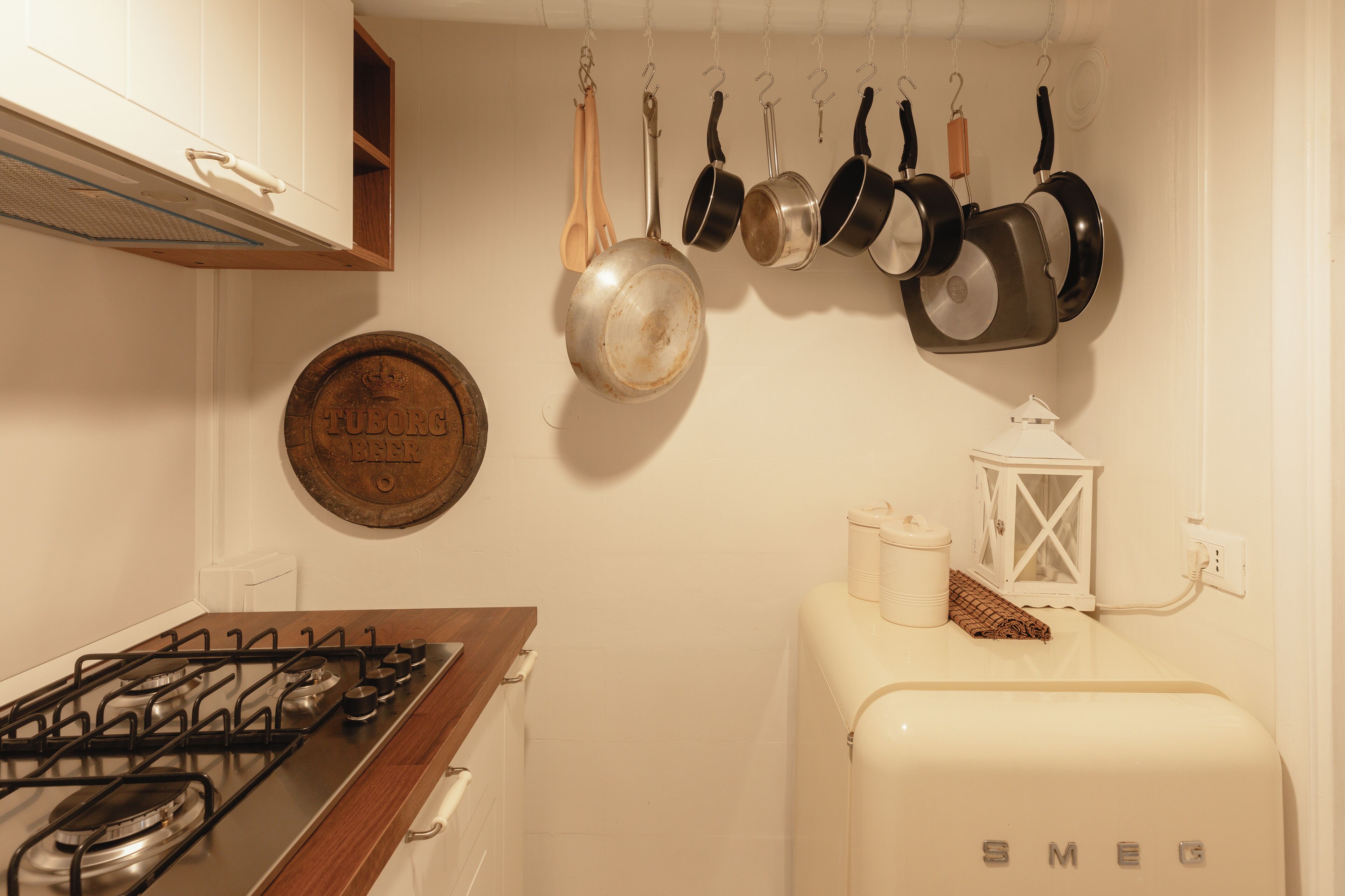 A kitchen with a gas stove, hanging pots, a vintage sign, and a white refrigerator.
