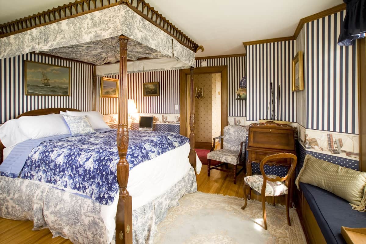 A bedroom with a four-poster bed, a desk, a chair, and a sofa.