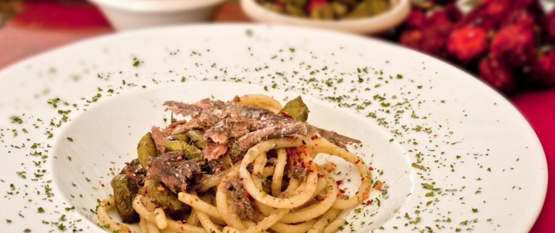 Un piatto di pasta con carne e verdure, guarnito con erbe aromatiche.