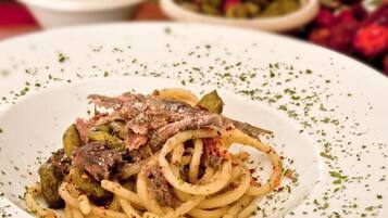 Un piatto di pasta con carne e verdure, guarnito con erbe aromatiche.