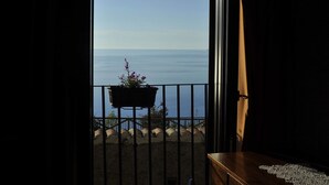 Un balcón abierto con vista al mar, un banco de madera y una planta en maceta.
