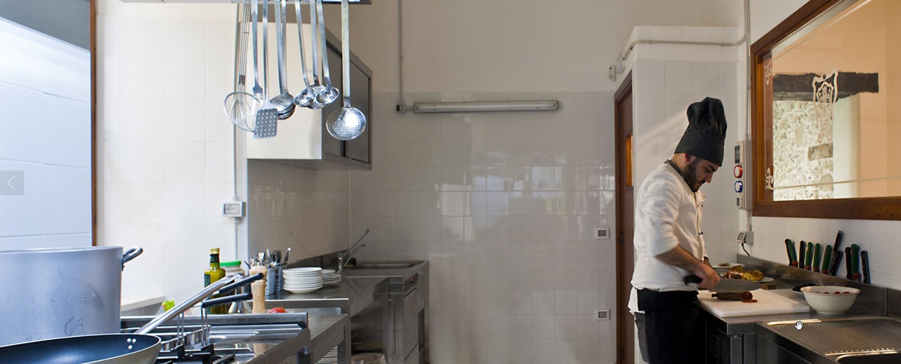 A chef in a modern kitchen with stainless steel appliances, hanging utensils, and a clean, organized workspace.