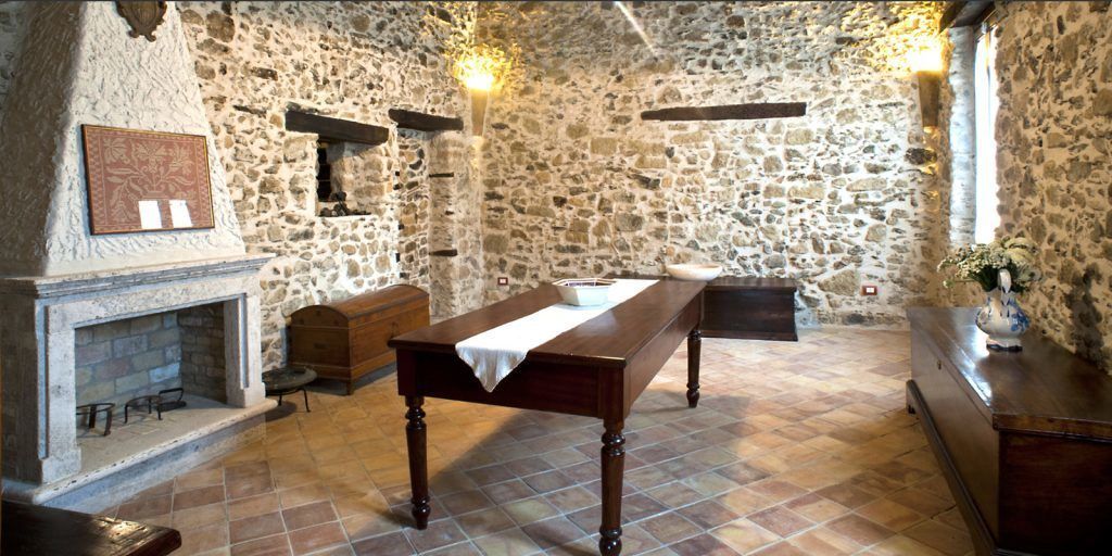 A stone-walled room with a fireplace, a long wooden table, and a bench.