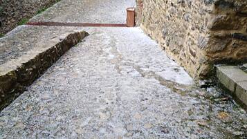 A cobblestone alley with stone walls on either side, leading to a building entrance.