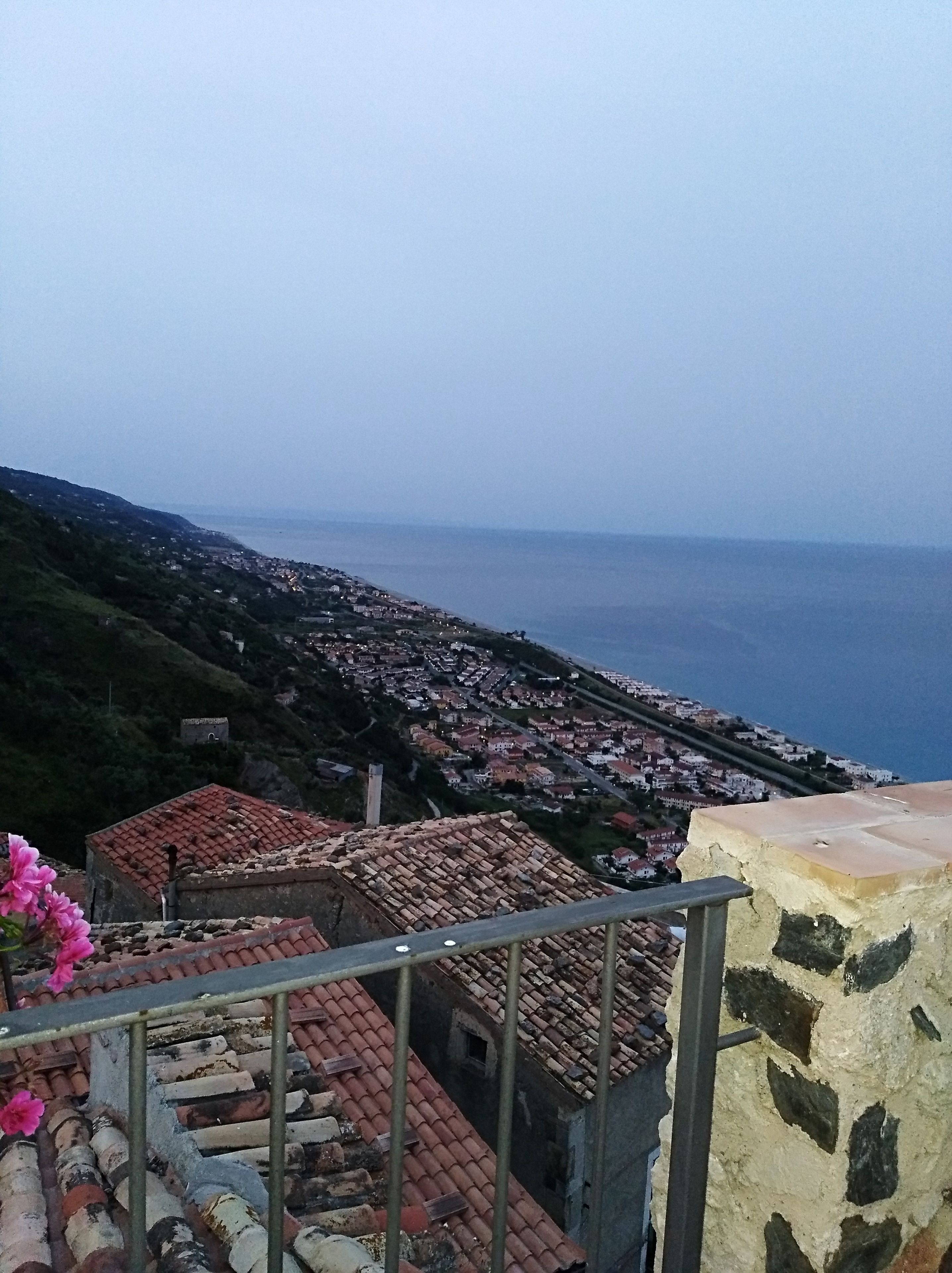 Un pueblo costero con edificios de tejas color terracota, una vista despejada del mar y una escalera que desciende hacia el pueblo.