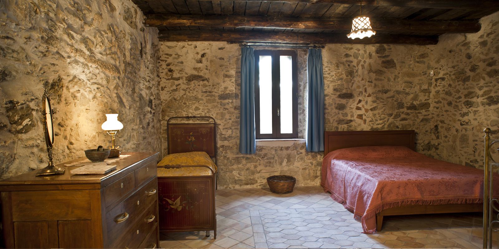 Une chambre rustique avec un lit en bois, une commode, une lampe et une fenêtre ornée de rideaux bleus.