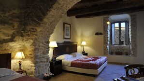Un dormitorio acogedor con pared de piedra, cama con colcha roja y blanca, dos lámparas de noche y ventana con vistas.