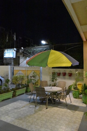 Un espace extérieur aménagé avec une table et des chaises, un parasol coloré et des plantes en pot.