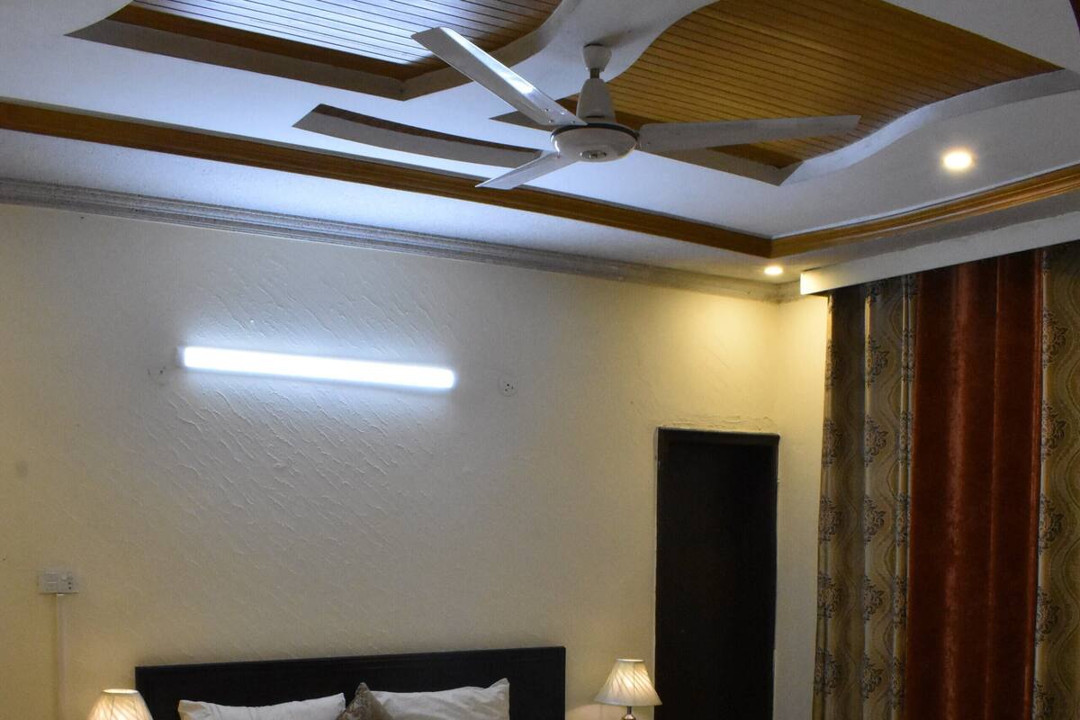A bedroom with a large bed, two bedside tables with lamps, a ceiling fan, and a door with curtains.