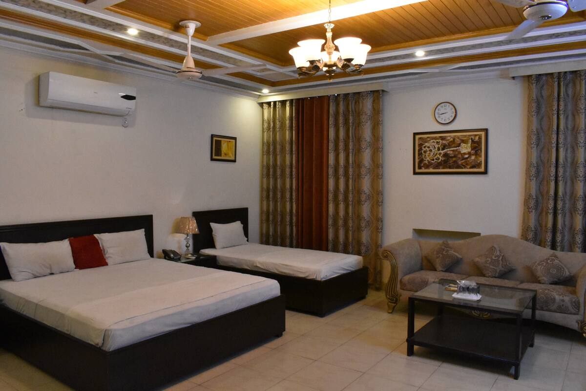 A hotel room with two beds, a sofa, a coffee table, a clock, and curtains.