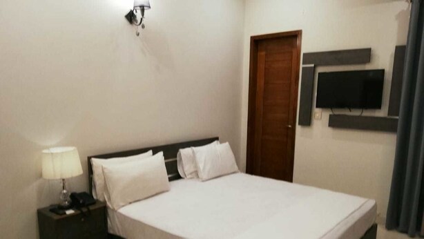Un dormitorio ordenado con cama, mesita de noche, lámpara y televisor de pantalla plana montado en la pared.