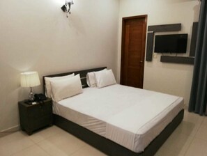 Un dormitorio ordenado con cama, mesita de noche, lámpara y televisor de pantalla plana montado en la pared.