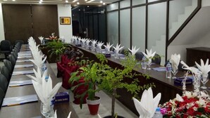 Un salón de conferencias con una larga mesa, sillas, plantas en macetas y una escalera.