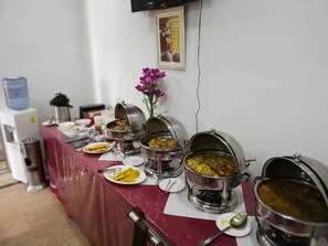 Une table de buffet garnie de différents plats, avec un distributeur d’eau en arrière-plan.