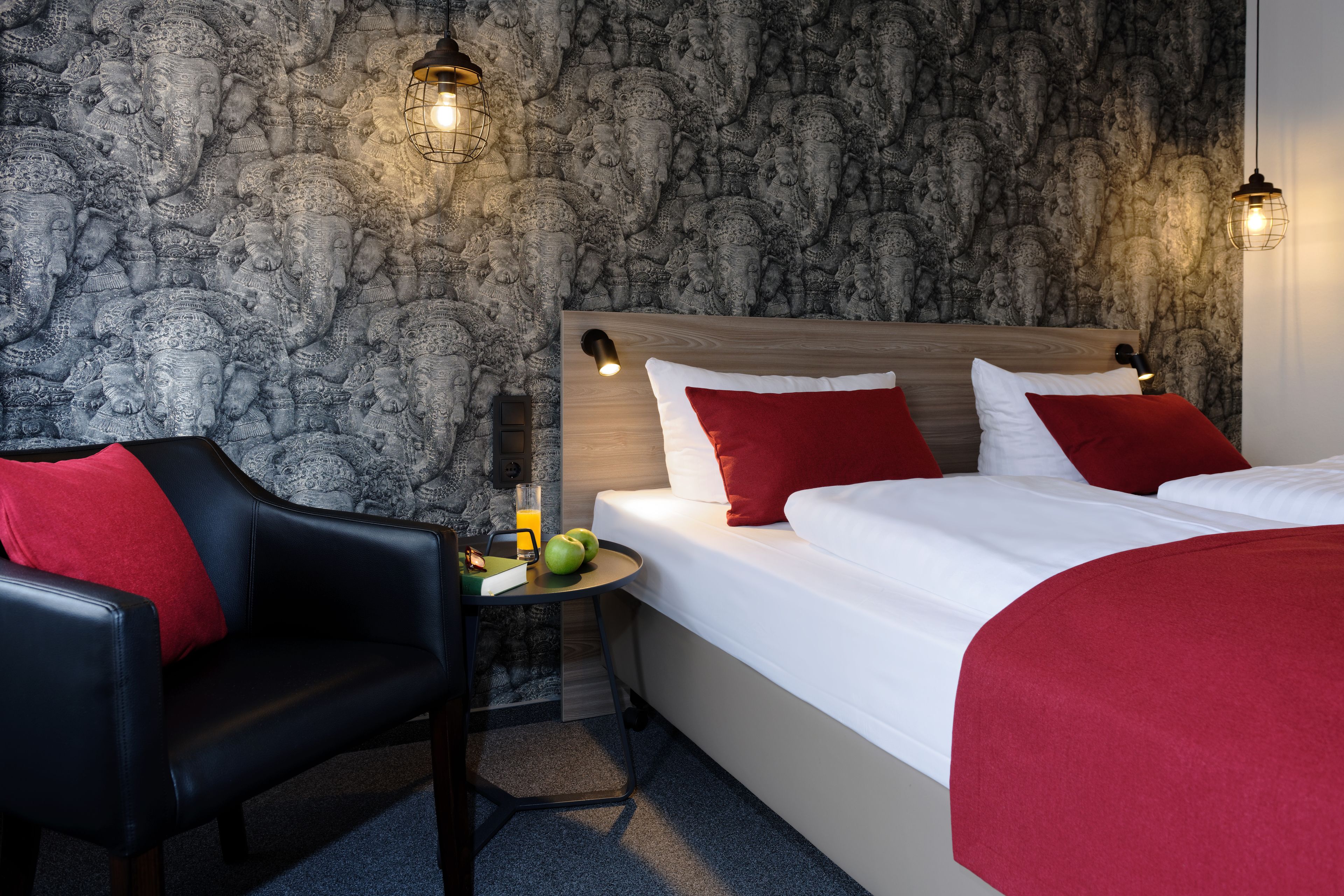 Une chambre d’hôtel avec un mur décoré d’un motif en pierre, une tête de lit en bois et une couvre-lit rouge et blanche.