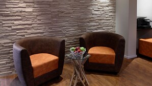 Two brown armchairs with orange cushions, a glass table with a fruit bowl, and a stone-textured wall. - Trend Hotel Oldenburg (Wiefelstede)