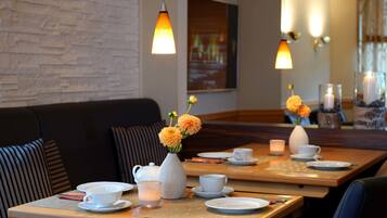 A restaurant with wooden tables, white tableware, and orange flowers in vases.
