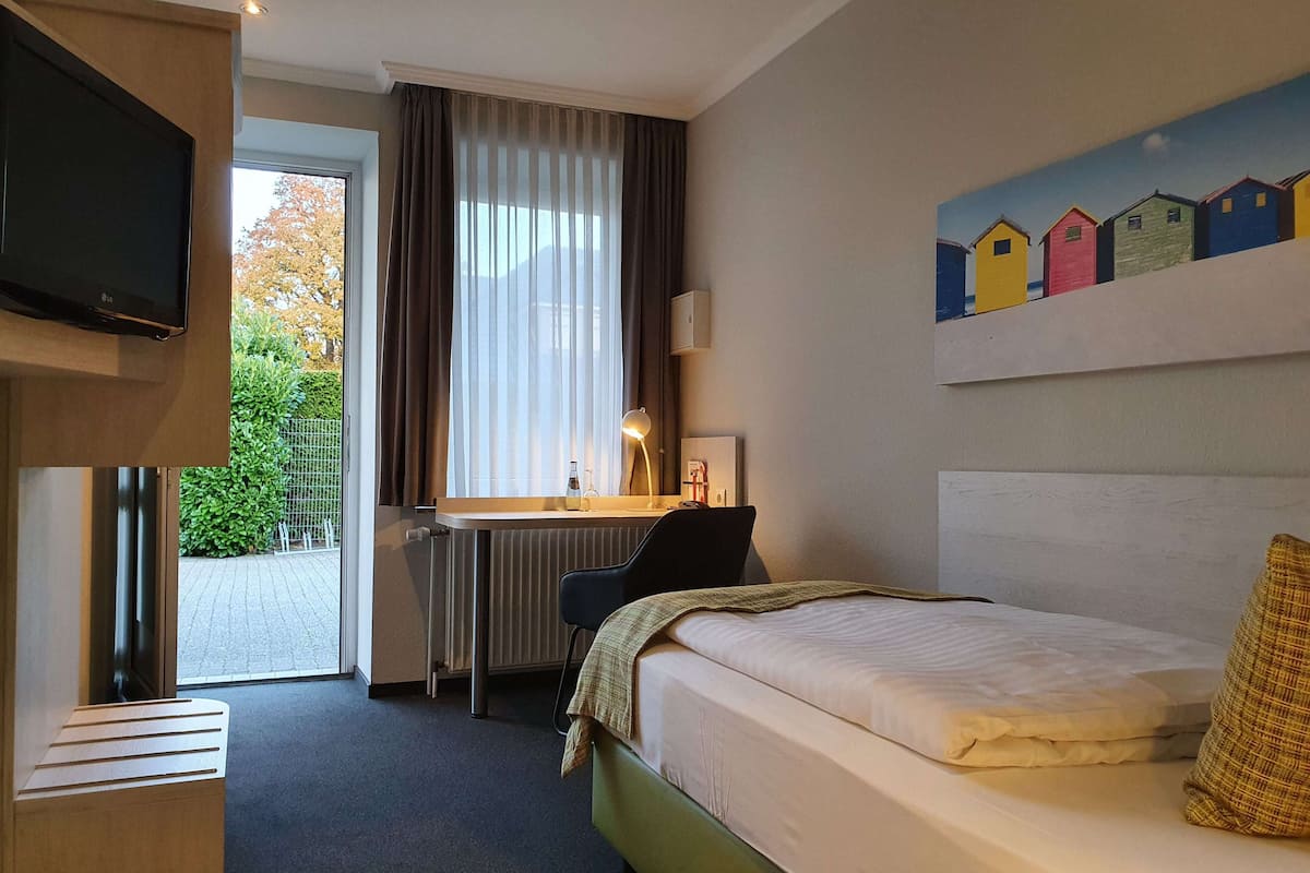 A hotel room with a bed, a desk, a chair, a TV, and a window with curtains.