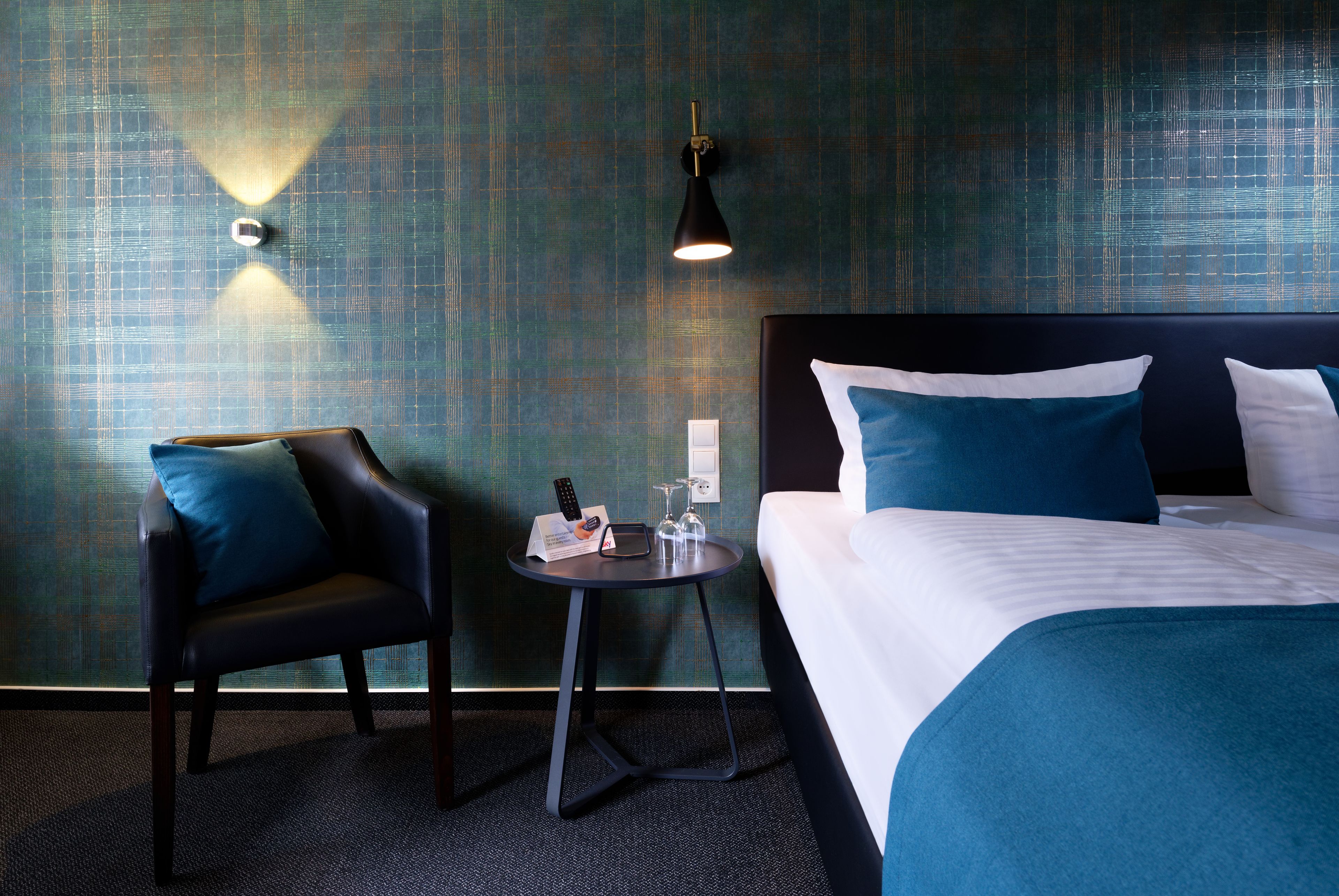 Une chambre d’hôtel avec un lit, une chaise, une petite table et une lampe fixée au mur.