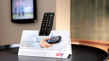 Une télécommande posée sur un support, avec une pancarte indiquant : « Une meilleure expérience de divertissement pour nos clients – Sky dans chaque chambre. »