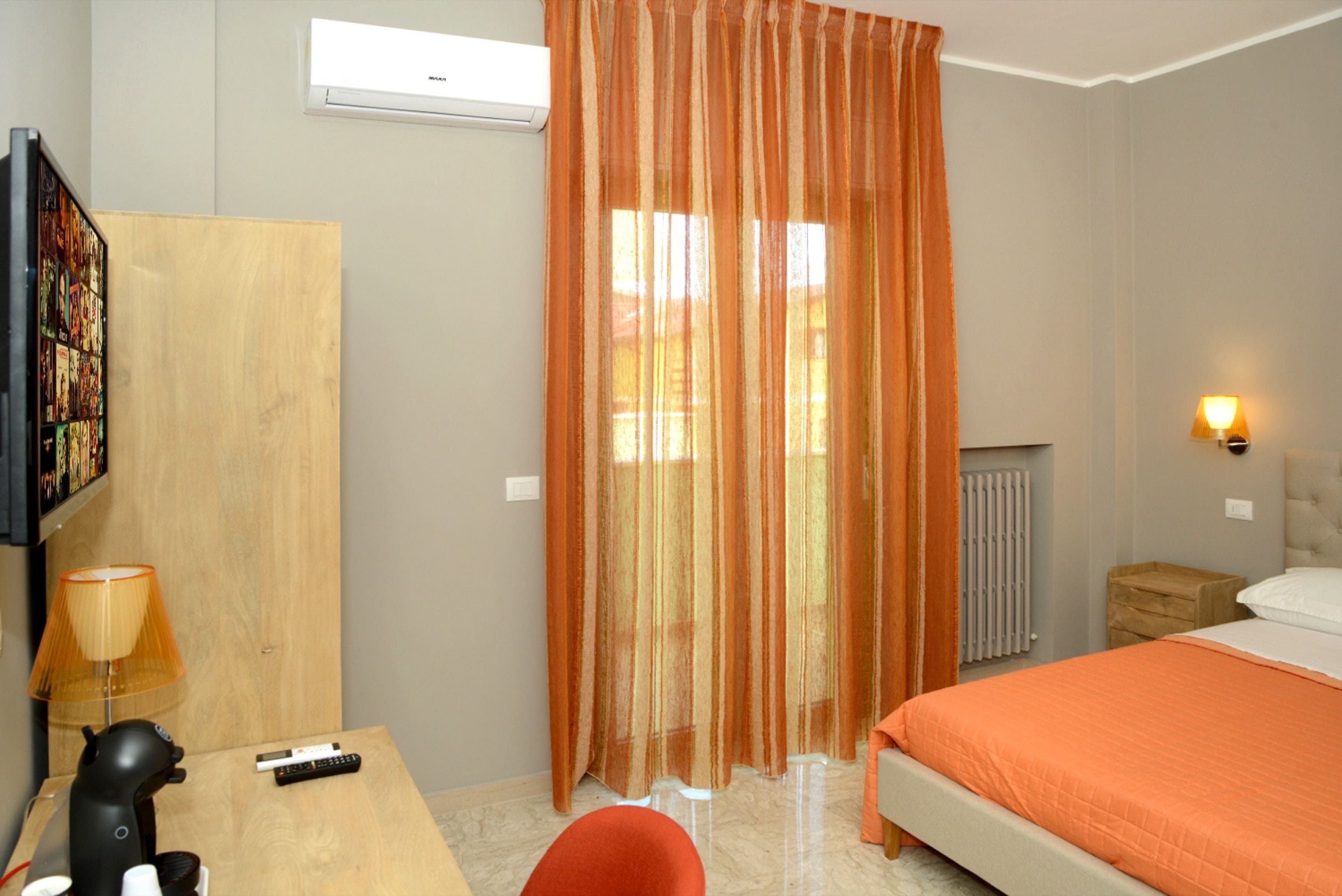 Une chambre d’hôtel avec un lit, un bureau avec une lampe, une chaise, une télévision et une fenêtre avec des rideaux.