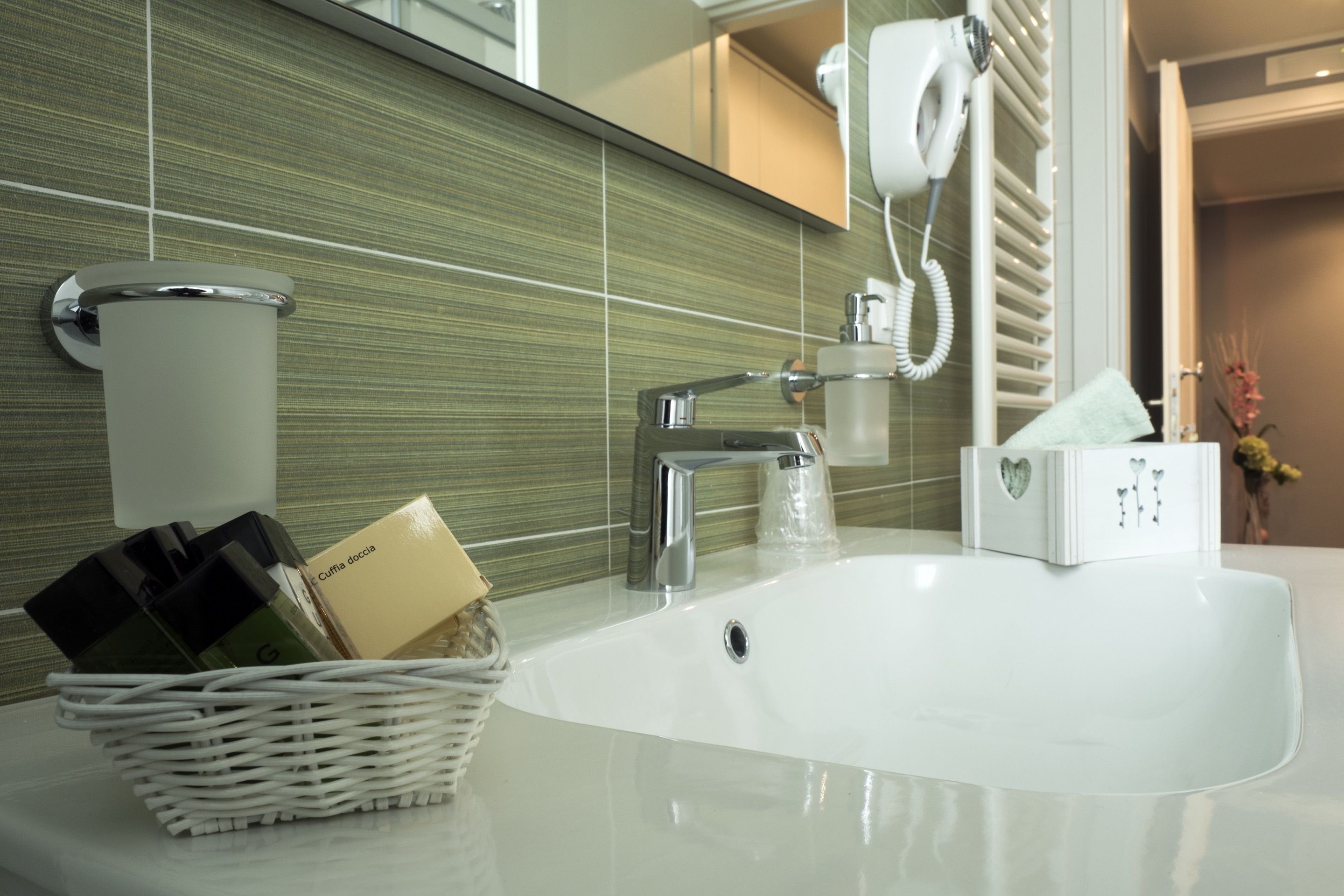 A modern bathroom with a white sink, chrome faucet, and a towel dispenser.