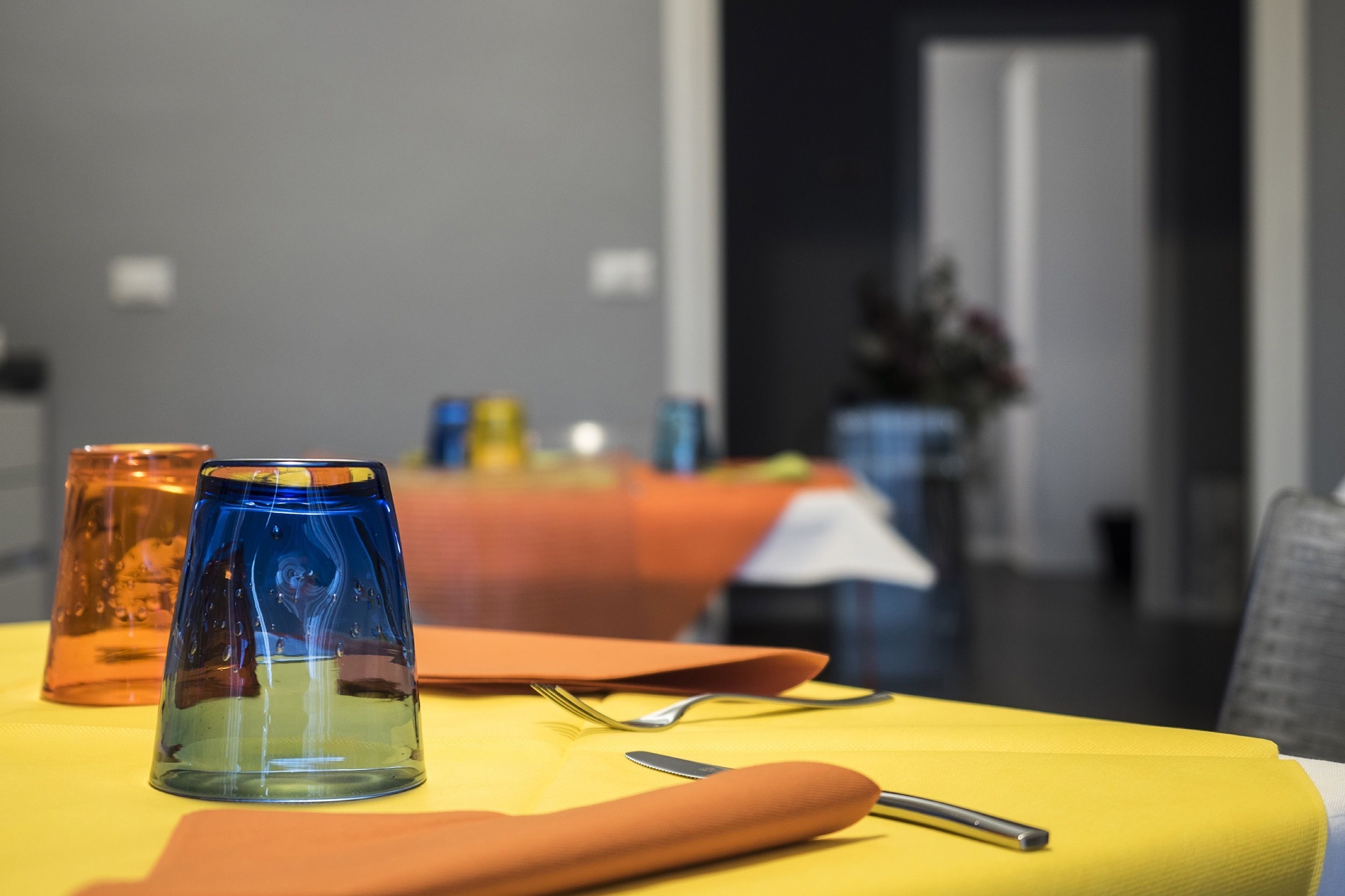 Una mesa de comedor con mantel amarillo, dos candelabros de vidrio y un tenedor y cuchillo sobre la mesa.