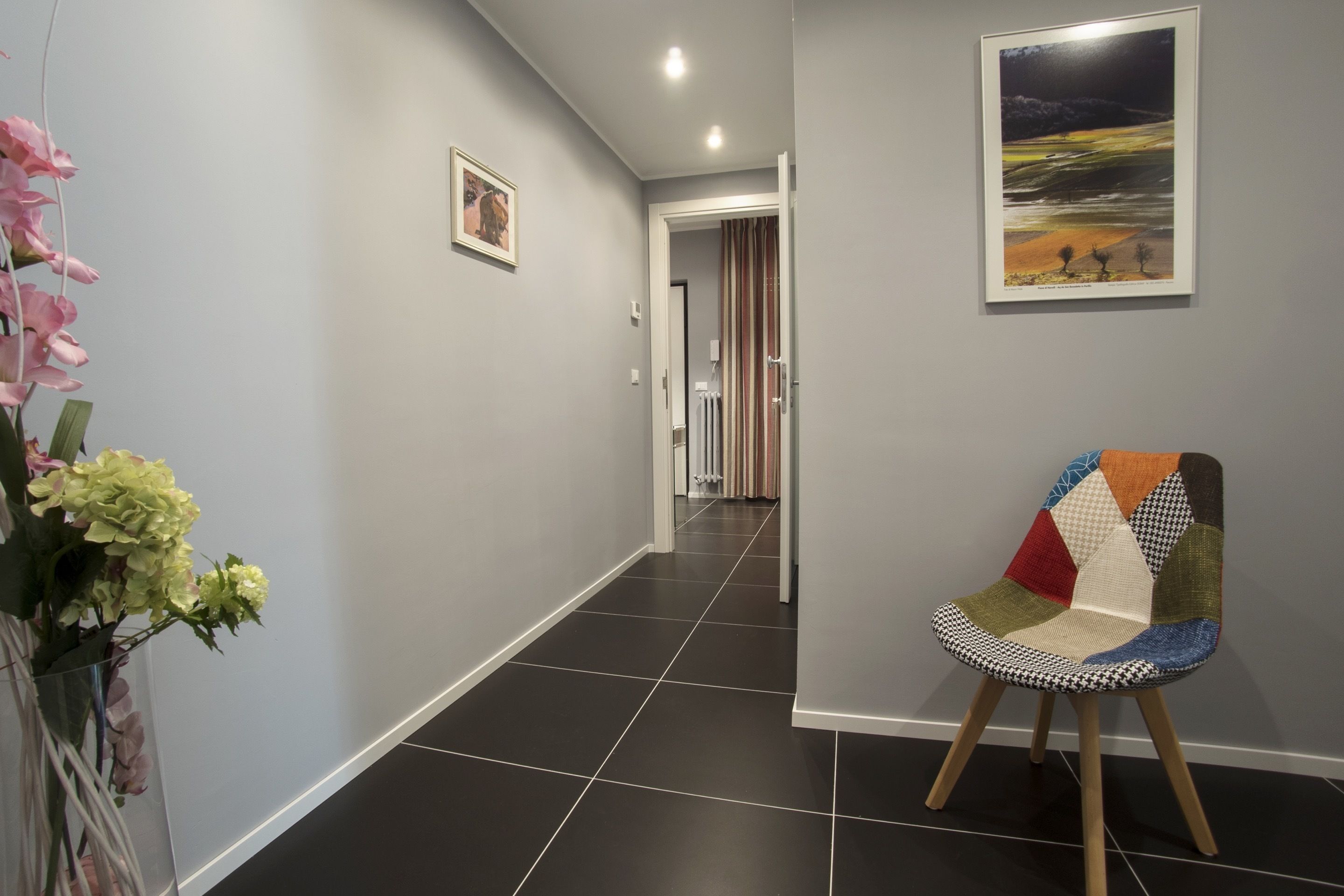 A hallway with a chair, a vase of flowers, and a framed picture on the wall.
