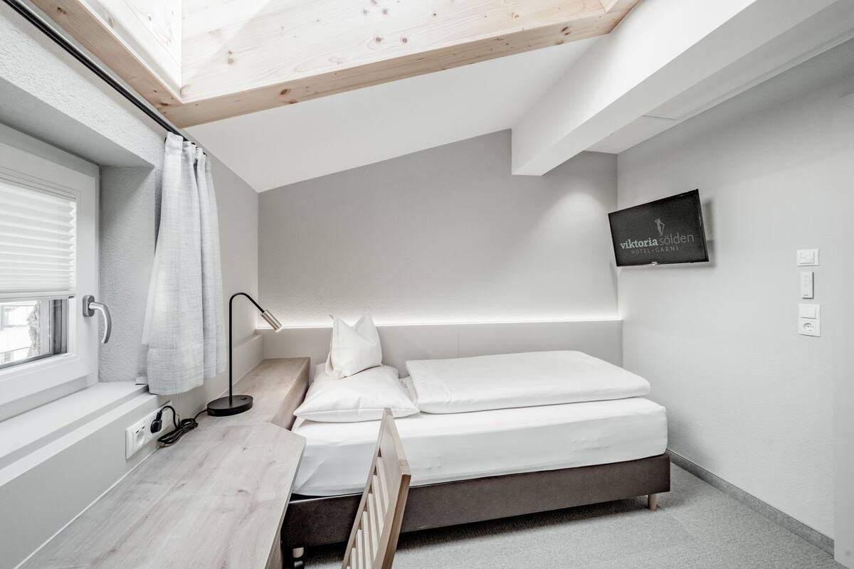 A modern bedroom with a skylight, a bed, a desk, and a TV on the wall.