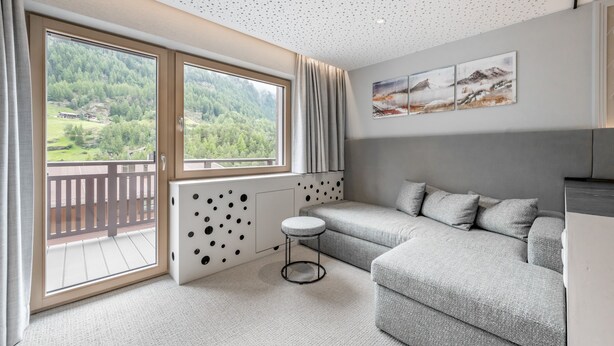 A modern room with a grey sofa, a small round table, and a large window offering a view of a forested area. - Viktoria Sölden (Soelden)
